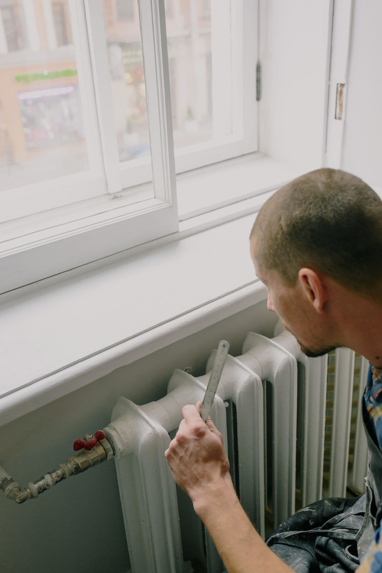 Handwerker nimmt Maß an einem Heizkörper in einer hellen Wohnung